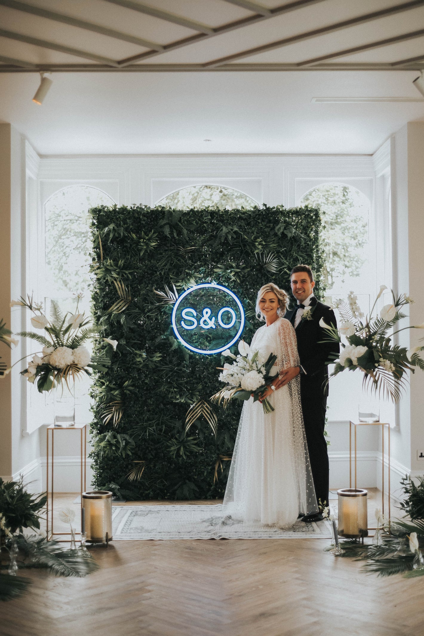 A bride and groom on their wedding standing in front of a ceremony backdrop with a custom neon sign for wedding by Wildfire Neon in Manchester, UK