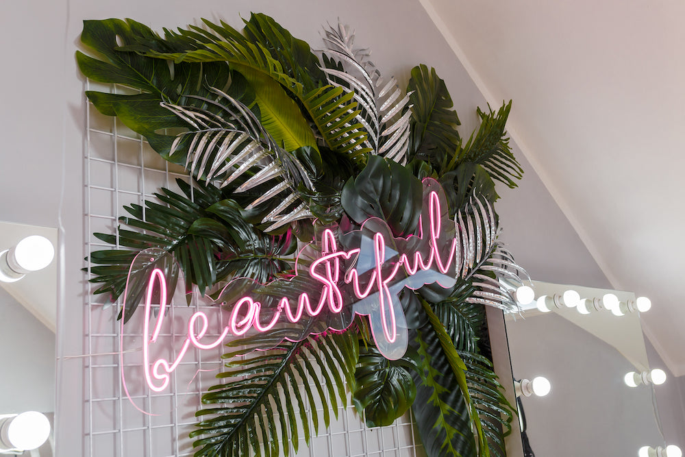 Neon sign spelling 'beautiful' surrounded by tropical leaves on a decorative wall