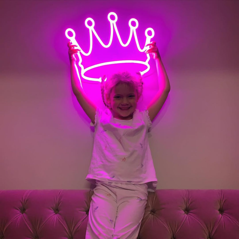 Child sitting on a pink couch with a neon crown light behind them