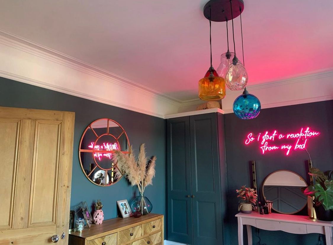 Wide image of a pink neon bedroom sign saying ‘so I start a revolution from my bed’